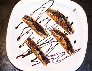 Üstünde çikolata sosu olan dört tabak sandviç. Sandviçler üçgen şeklinde kesiliyor ve beyaz bir tabakta düzenleniyor. Tabak bir masanın üzerine konur. Tabağa yayılmış çikolata sosu..