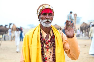 Pushkar, Rajasthan, Hindistan - 22 Aralık 2014: Sarı kostüm giymiş bir kadın elinde kase tutuyordu. Kadınlar altın bir başlık takıyor ve siyah bir peruğu var. Ayrıca çiçek çelengi takıyor..