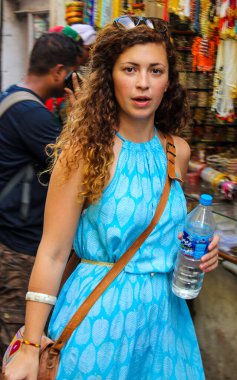 Pushkar, Rajasthan, Hindistan - 22 Aralık 2014: Mavi elbiseli bir kadın elinde bir şişe su tutuyor. Kahverengi kemer ve beyaz bir bilezik takıyor.