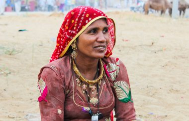 Pushkar, Rajasthan, INDIA - 22 Aralık 2014: Kırmızı eşarp takan Hintli ya da Rajasthanlı bir kadın yerde oturur. O gülümsüyor. Arka planda iki at var.