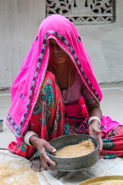 Pembe sari giyen bir kadın bir kase pirinç tutuyor. O yerde oturuyor.
