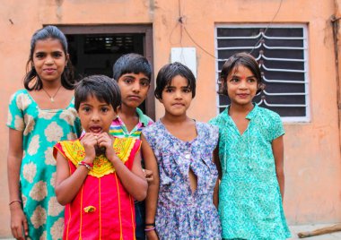 Bir grup çocuk bir evin önünde duruyor. Kızlardan biri kırmızı elbise giyiyor.