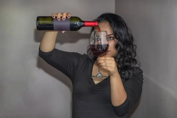 woman pouring red wine from bottle to a glass