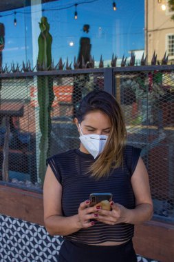 Zarif Meksikalı iş kadını cep telefonu kullanarak yüz maskesi takıyor.