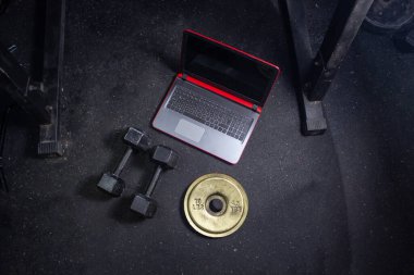 Spor salonunda halterler dizüstü bilgisayarın yanında ve demir disk ağırlık plakası. spor arkaplanı