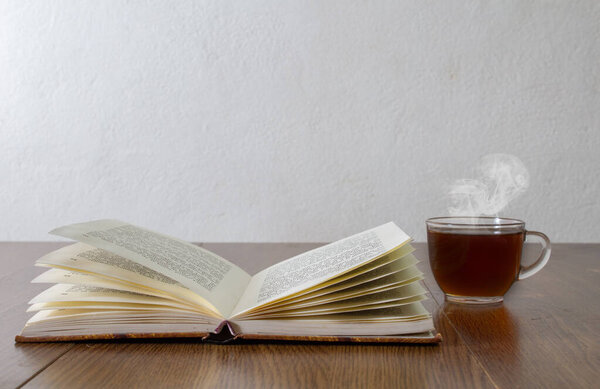 cup of coffee next to open book at home reader concept
