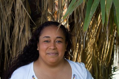 Geleneksel yerli kıyafetleri içinde kuru palmiye ağaçlarının önünde gülümseyen Meksikalı kadın. İspanyol.