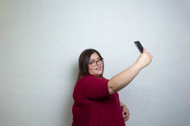 Şişman kadın cep telefonuyla izole edilmiş beyaz arka planda selfie çekiyor.