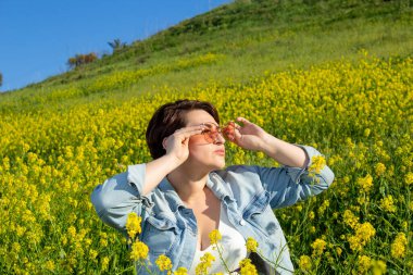 Güneş gözlüğü takan güzel bir manken bahar mevsiminde çiçeklerle dolu bir alanda doğanın tadını çıkarıyor.