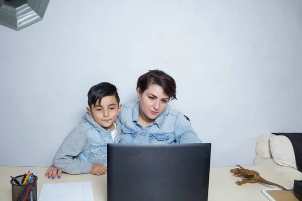 Anne ve küçük oğlu bilgisayar ekranından online ders izliyorlar. Meksikalı aile.