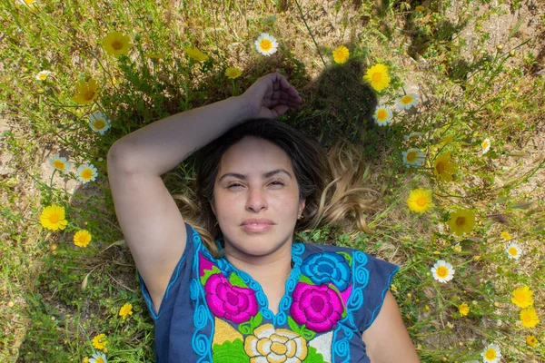 mature mexican woman lying in flower filled field wearing traditional mexican clothing