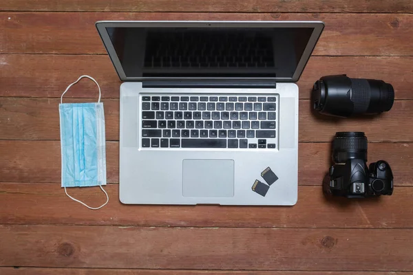 photographer\'s desk with photographic equipment, with camera, lenses, laptop and face mask for pandemic