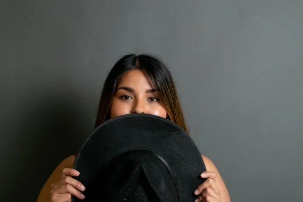 creative portrait of beautiful mexican woman covering her face with fedora hat. latin