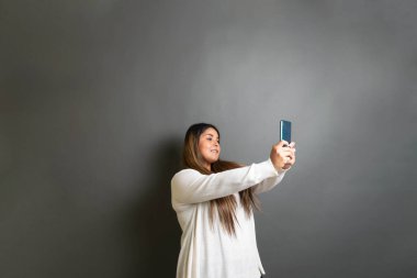 Güzel, tombul, İspanyol bir kadın cep telefonuyla selfie çekiyor.