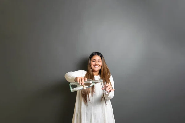 young mexican woman serving shot of tequila, vodka or mezcal from bottle