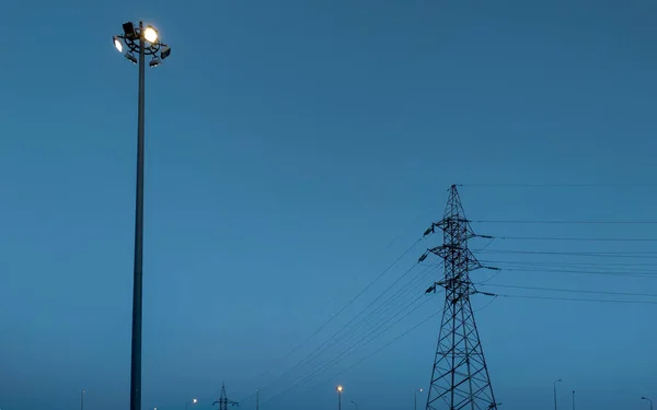 Hochspannungsleitung Mit Metallträger Und Laternenpfahl Mit Leuchtlampe Vor Blauem Abendhimmel — Stockfoto