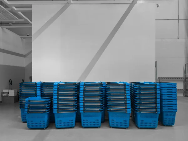 Büyük bir alışveriş merkezinde yığılmış bir sürü mavi sepet. Üstlerinde yazı için yer var. Süpermarket sepetleri müşterileri besler.