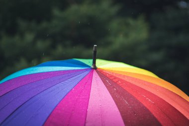 Gökyüzünden gökkuşağı renkli bir şemsiyeye yağmur damlaları düşer. Hafif yağmur. Bulutlu hava.