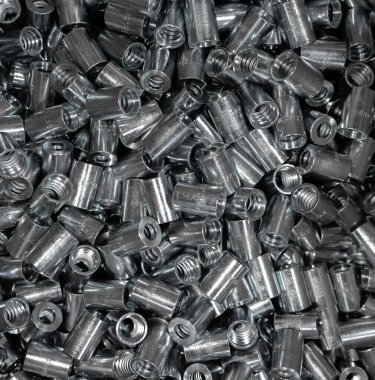 A background of many short female threaded metal fittings for connecting pipes. Lots of loose fittings. Plumbing equipment. View from above.