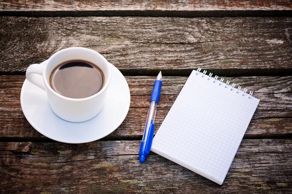 Tazza di caffè, blocco note e penna su sfondo di legno — Foto Stock