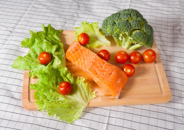 Salmone fresco con pomodori, broccoli e insalata su un tagliere Foto Stock