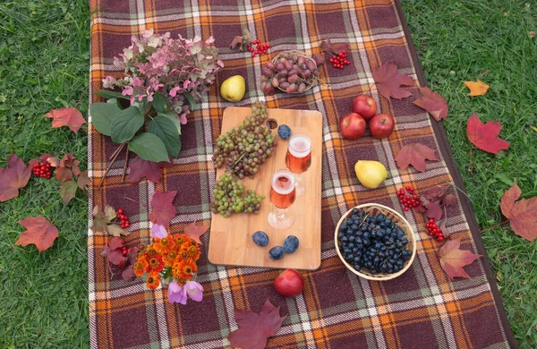 Autumn outdoor picnic setting with glasses of rose champagne, fruits and flowers. Top view.