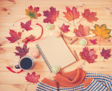 Boş defter, bir fincan sıcak kahve, sonbahar akçaağaç yaprakları, badem kurabiyeleri ve ahşap masada ev yapımı sıcak süveter. Üst görünüm, alanı kopyala.