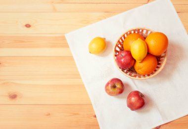Portakallar, elmalar ve limonlar sepetin içinde ahşap masada beyaz peçete üzerinde. Üst görünüm, alanı kopyala.