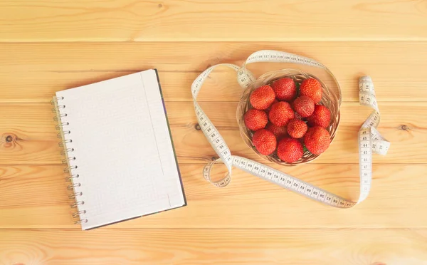 测量磁带 柳条篮新鲜草莓和记事本木制背景 顶部视图 复制空间 — 图库照片