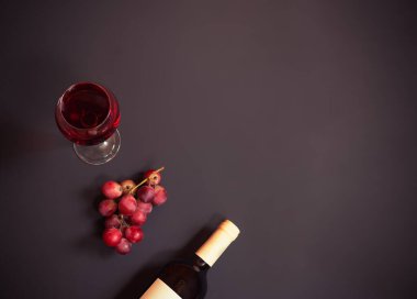 Bir kadeh kırmızı şarap, mor üzüm ve koyu arkaplanda bir şişe kırmızı şarap. Kopyalama alanı olan üst görünüm.