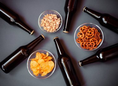 Kahverengi cam bira şişeleri ve gri arka planda bira atıştırmalıkları. Üst görünüm.