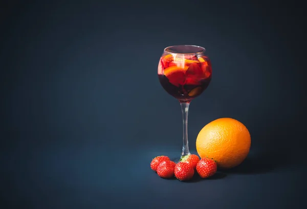 Red wine sangria with orange and strawberry in glass, orange and strawberry near. Dark background. View with copy space.