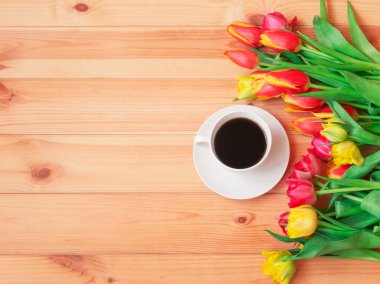 Beyaz kahve fincanı ve ahşap masanın kenarındaki renkli taze bahar laleleri. Üst görünüm, alanı kopyala.