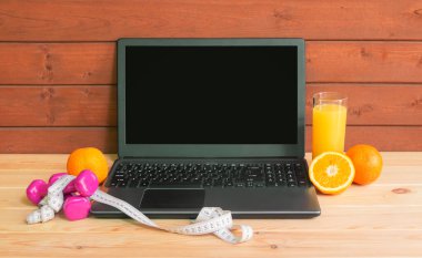 Dizüstü bilgisayar, dambıl, mezura, bir bardak portakal suyu ve taze portakal. Egzersizler, sağlıklı yiyecekler, online fitness eğitimi, evde kalmak. Kopyalama alanı ile göster.