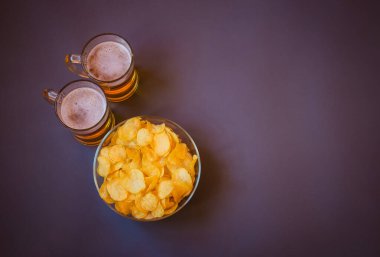 Fincanlar dolusu bira ve gri arka planda patates cipsi. Üst görünüm, alanı kopyala.