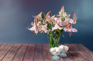 Pembe lekeli bej zambak buketi ve gri arka plandaki ahşap masada bir kase dondurma. Kopyalama alanı ile göster.