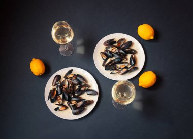 Beyaz tabaklar, midyeler ve koyu arkaplanda beyaz şarap bardakları. Üst görünüm.