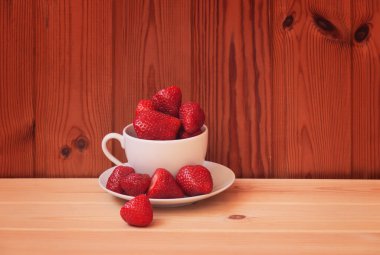 Tahta masada beyaz fincanda taze çilekler. Kopyalama alanı ile göster.