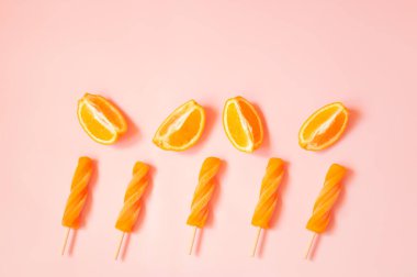 Pembe arka planda spiral turuncu buzlu şeker ve taze portakallar. Üst Manzara. Boşluğu kopyala.