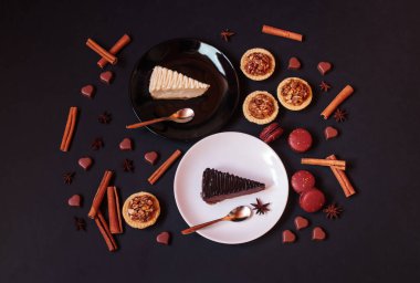 Çikolata ve klasik peynirli kekler, çikolatalı kurabiyeler, cevizli kekler, baharatlar ve koyu arkaplanda kalp şeklinde çikolatalı şekerler. Üst görünüm.