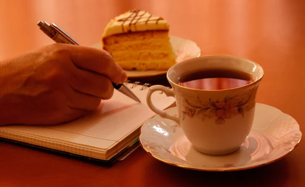 Escritura a mano en cuaderno, taza de té y trozo de pastel — Foto de Stock