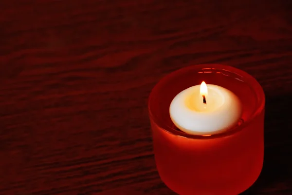 Одна свеча в оранжевом стекле подсвечника на темном деревянном столе — стоковое фото