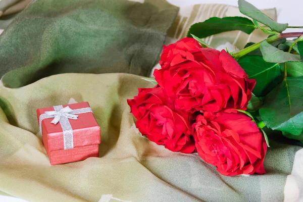 Rote Geschenkschachtel und drei rote Rosen auf grünem Seidenschal — Stockfoto