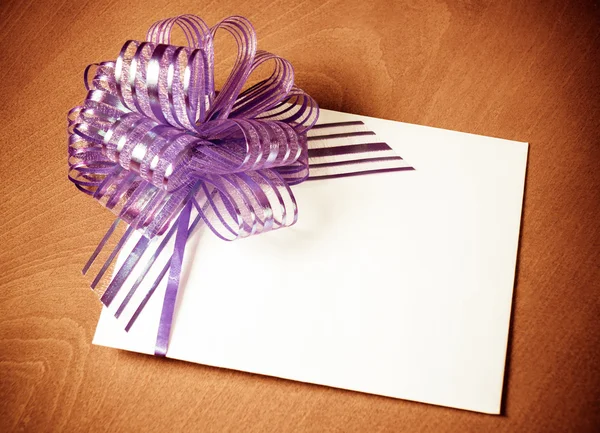 Close up of a note card with violet bow on wooden background. Vi