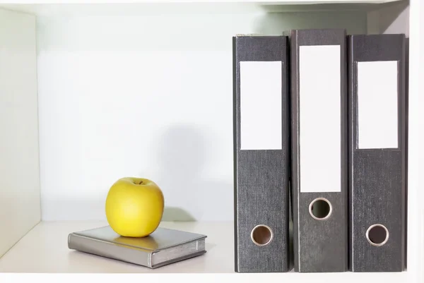 Folders for documents, planner and green apple on a book shelf — Stock Photo, Image