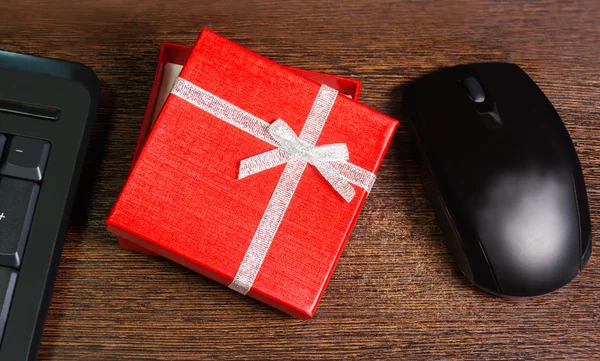 Composition with red gift box,  mouse and keyboard laying on woo