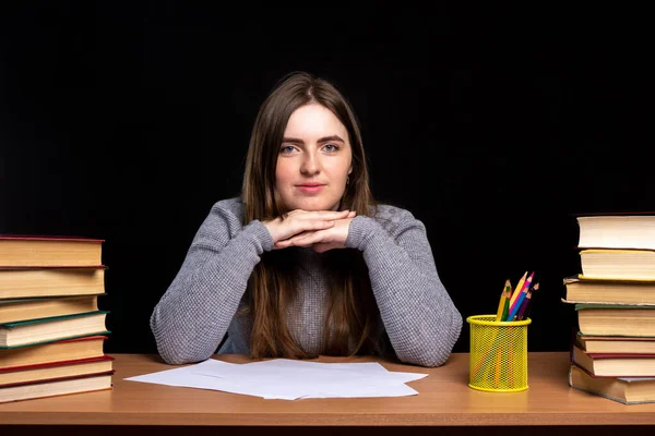 Ofiste ya da evde kitap ve belgelerle bir masada oturan genç bir kadın. Kameraya bak. Öğrenci sınava hazırlanıyor..