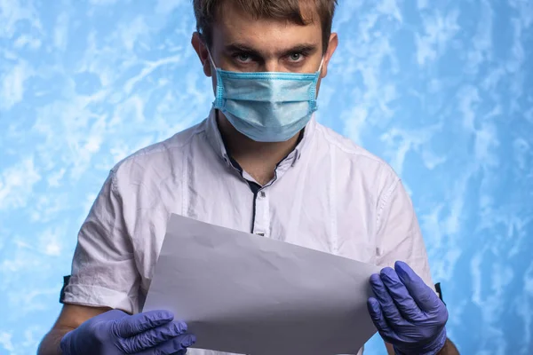 young man in a medical mask and gloves reads a document. the doctor observes safety measures during quarantine. individual protection means.