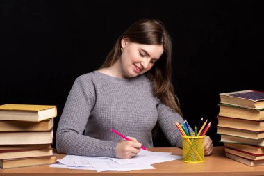 Genç bir kız öğrenci siyah duvar arka planında kitaplarla bir masada oturuyor. İş kadını evrakları gülümseyerek imzalar. Karantinada ev ödevlerinde ve okulda zorlanıyorsun. Avrupa görünümü