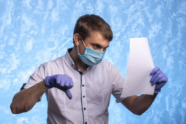 Tıbbi maskeli ve eldivenli genç adam bir belge okuyor. Doktor karantina sırasında güvenlik önlemlerine dikkat eder. bireysel koruma.
